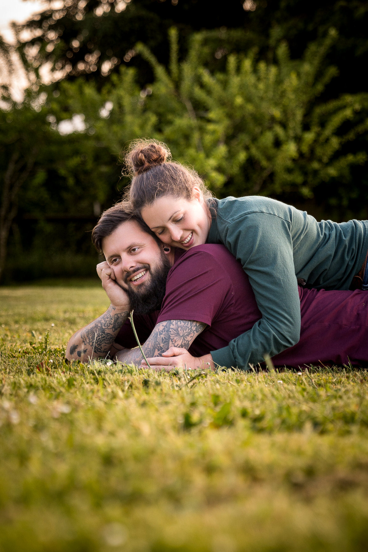 Emily and Dakota laughing during a casual engagement photo shoot, with Emily lying on Dakota's back on the ground, showcasing their genuine joy and connection, captured by Dan Berger Photography