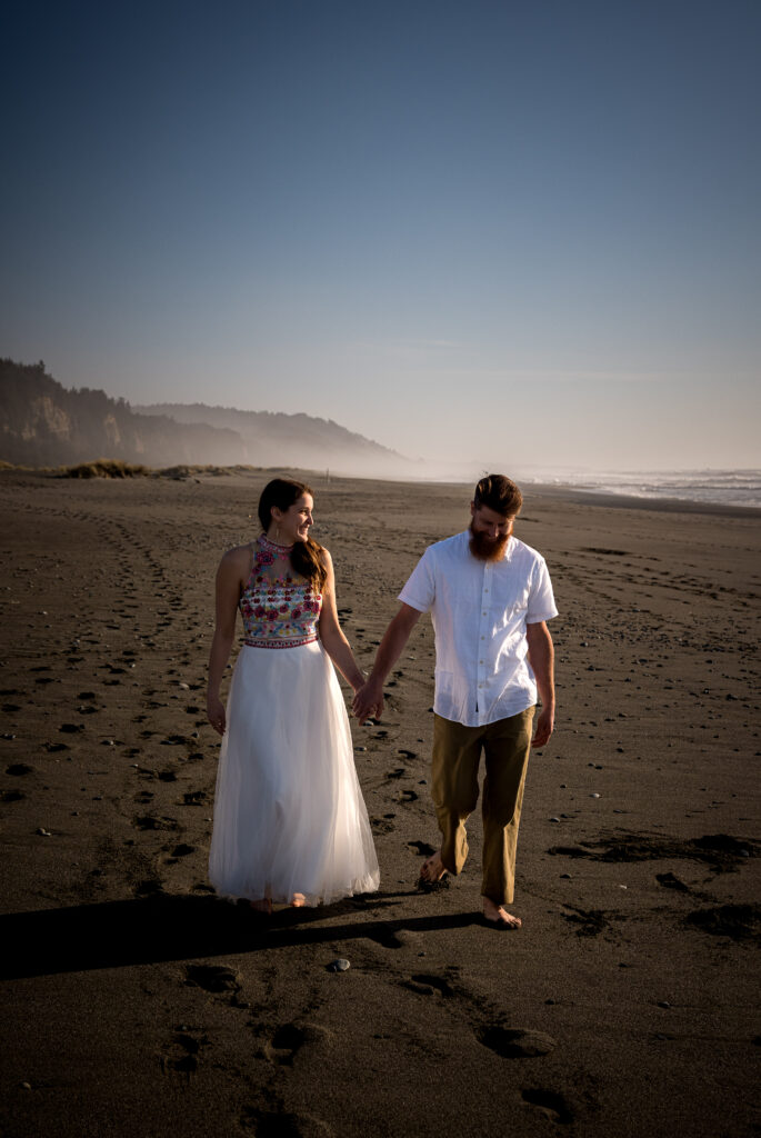 Lesley and Bryce holding hands during their beach engagement session at sunset – captured by Dan Berger Photography.