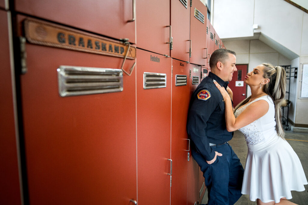 Alesha and David share a romantic moment during their firefighter-themed engagement session, standing in front of vintage red lockers.