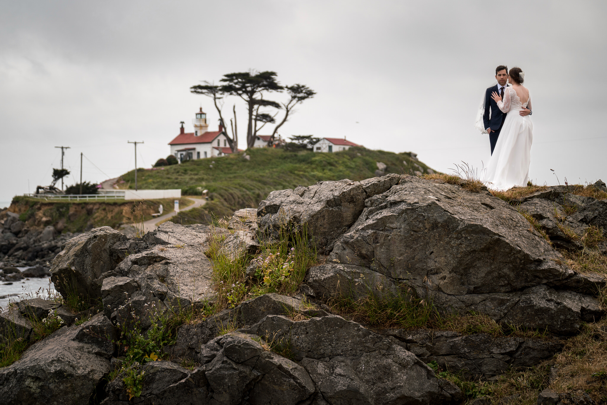 Bride and groom on a rocky coastal bluff overlooking a lighthouse in Crescent City