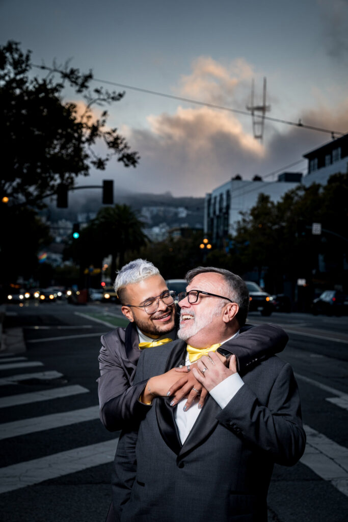 Husbands laughing together on a San Francisco street with fog rolling in near Swedish American Hall