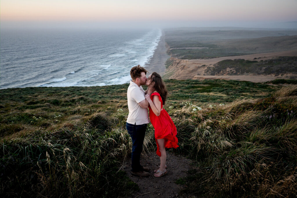 Couple kissing on grassy cliff overlooking the coastline at Point Reyes