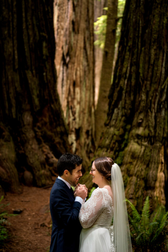 Bride and groom holding hands during a first look between towering redwoods