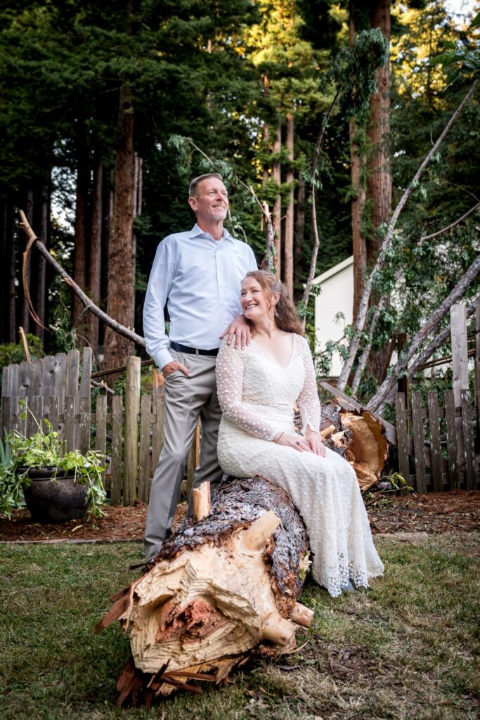 Bride and groom sitting on a fallen redwood tree in a backyard wedding ceremony