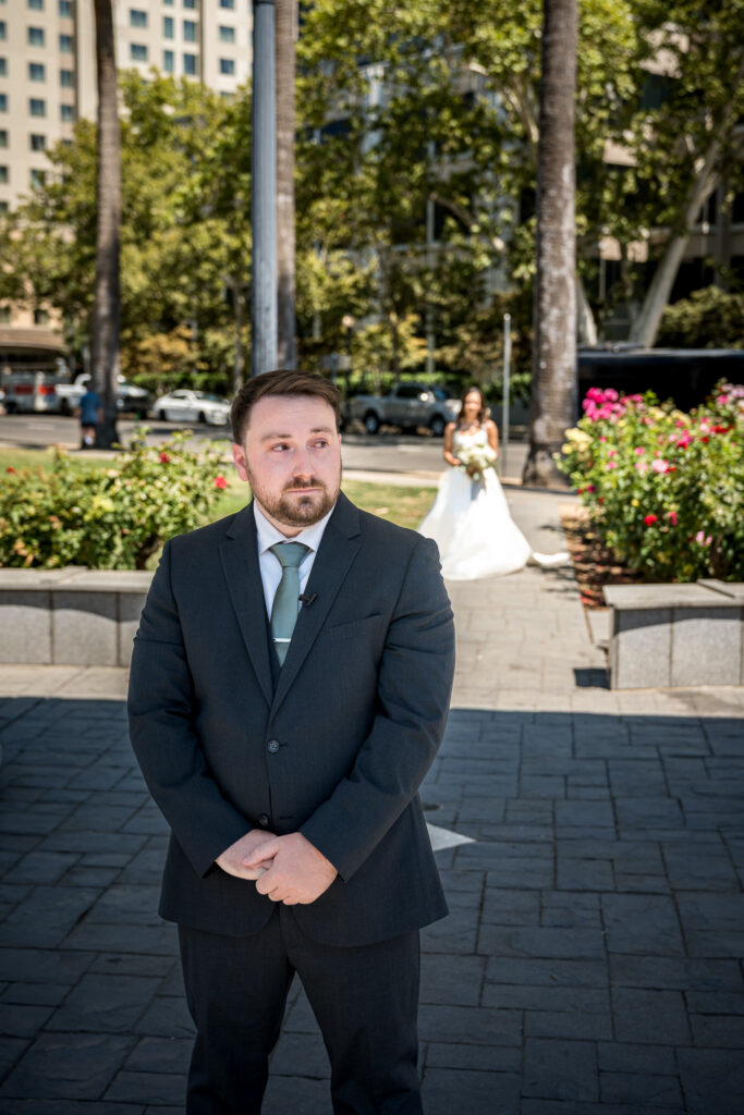 Groom waiting for a first look with bride approaching through the Capitol Park rose garden