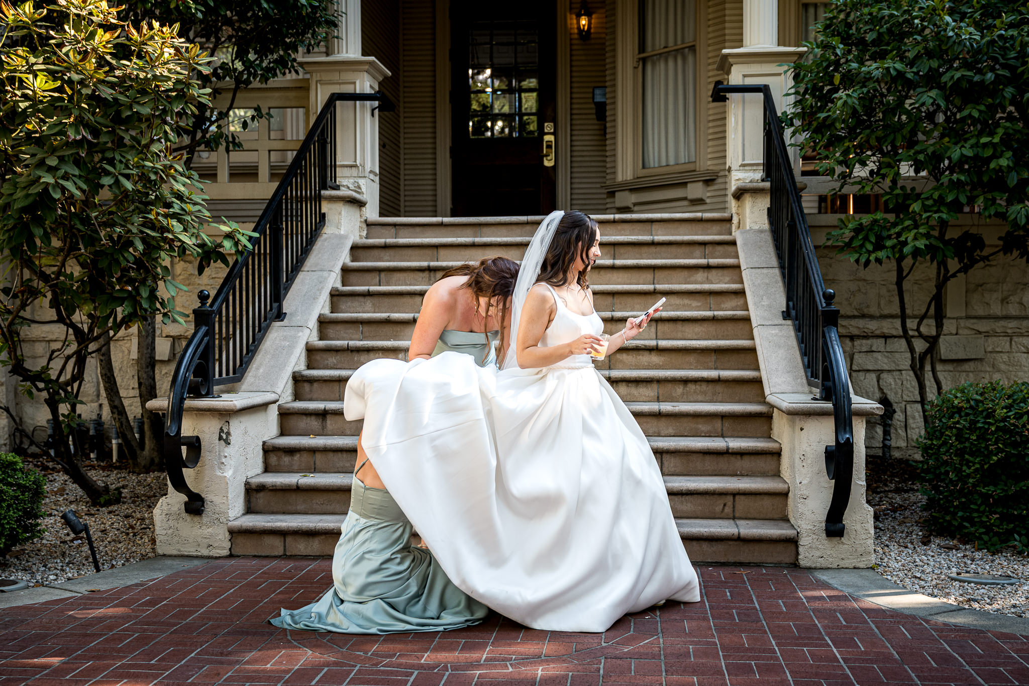Bride's sisters bustling her dress on the front steps of The Sterling Hotel