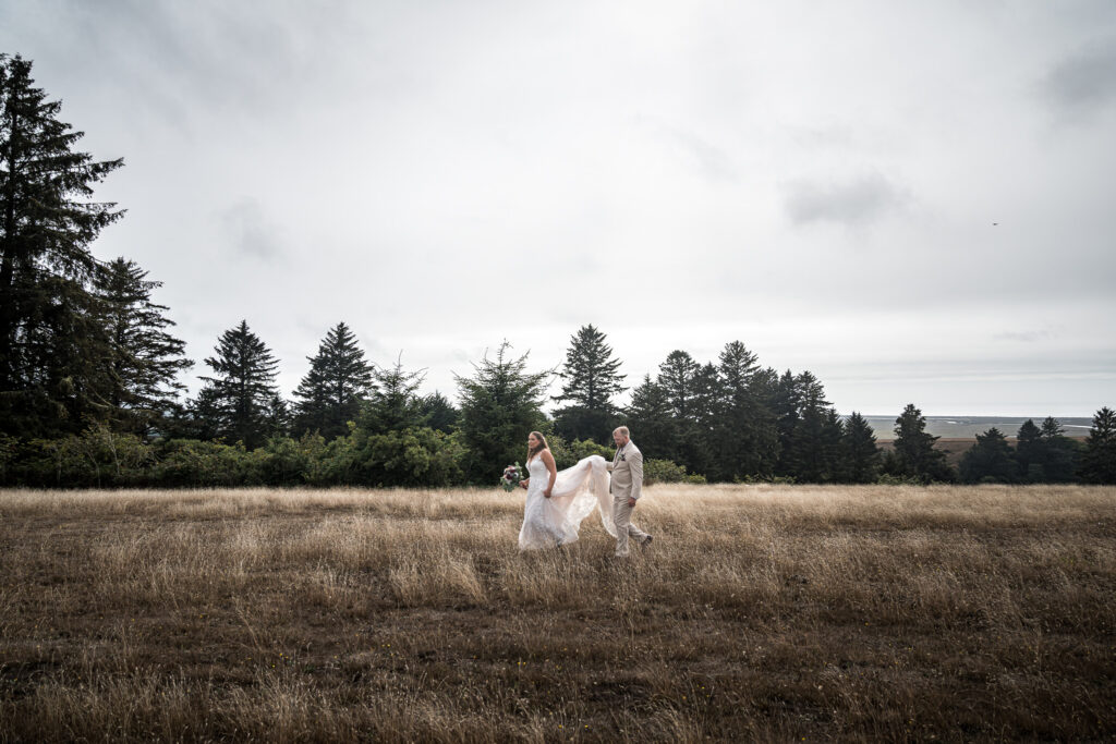 Bride and groom walking through a wind-swept field at North Coast Hitching Post overlooking the coastline