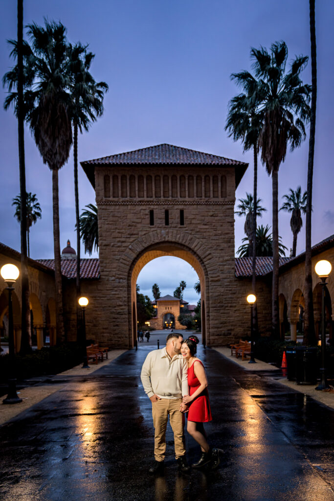Woman in red dress standing under archway at Stanford at twilight