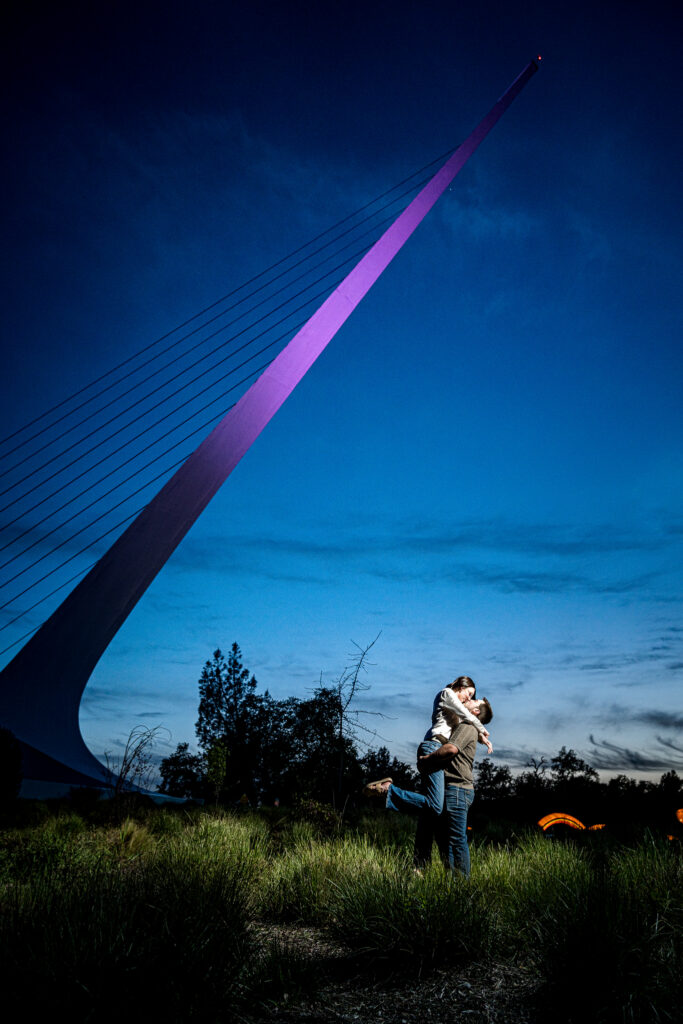 Couple embracing during blue hour beneath the Sundial Bridge's illuminated pylon, Turtle Bay