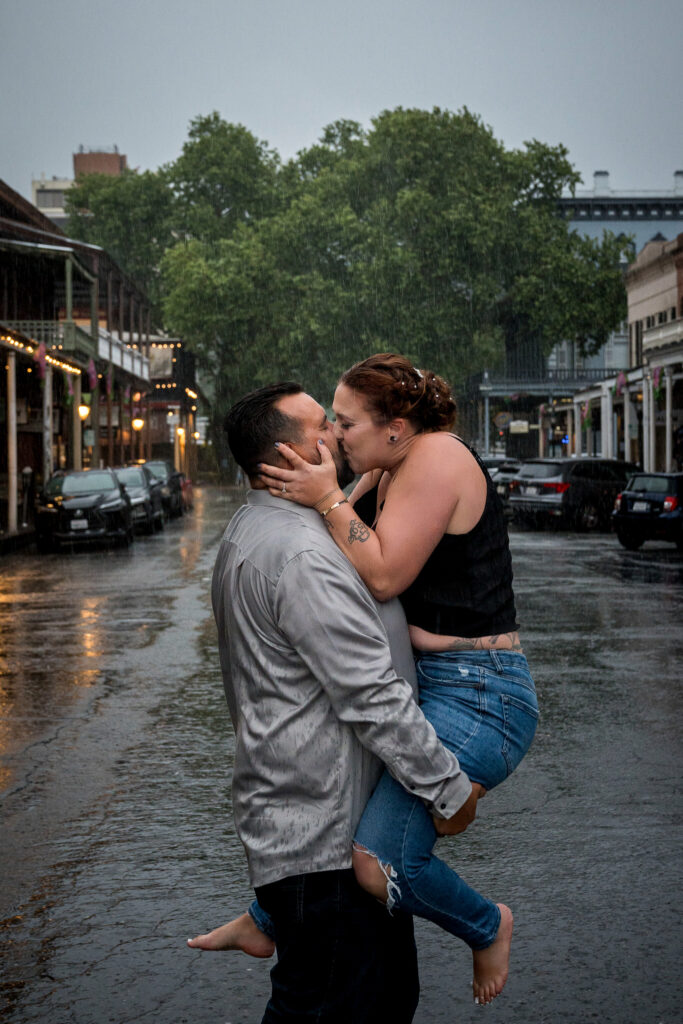 Man lifting woman for a kiss in the pouring rain on an Old Sacramento street