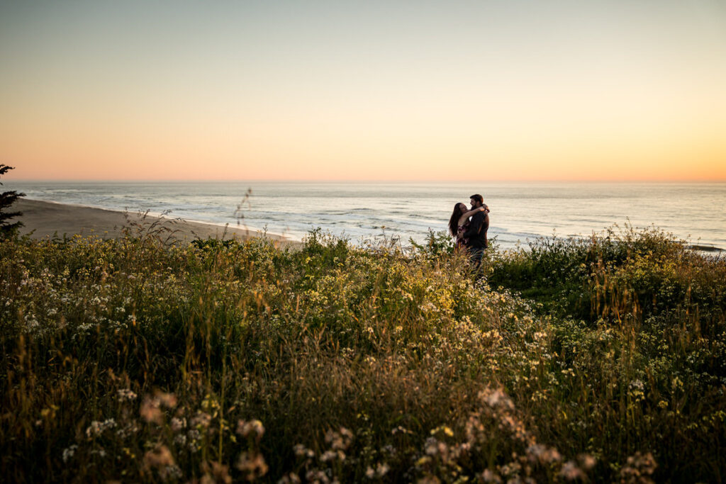 Emily and Dakota embracing in a serene sunset moment, surrounded by wildflowers overlooking the ocean in Loleta, creating a romantic and picturesque setting that captures the essence of their love, photographed by Dan Berger Photography.