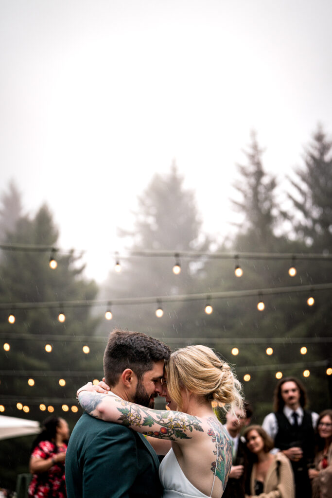 Bride and groom sharing their first dance at Ridgefield in Arcata, surrounded by warm string lights and an intimate crowd, with the soft fog of the evening creating a magical atmosphere.