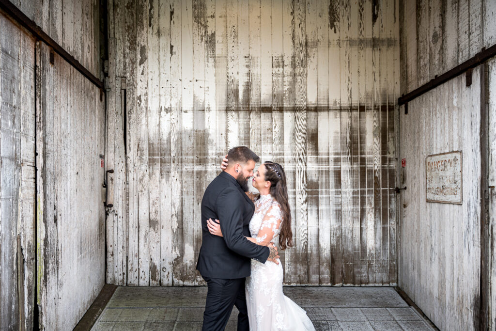 Bride and groom sharing a romantic moment at the North Coast Hitching Post in Loleta, with rustic barn doors and lush greenery providing a charming backdrop.