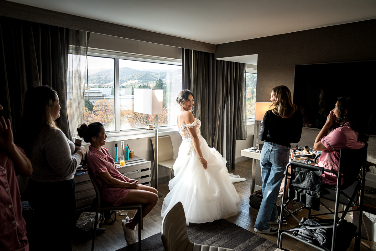 Bride revealing her wedding dress to her bridesmaids at the AC Hotel in Pleasanton.