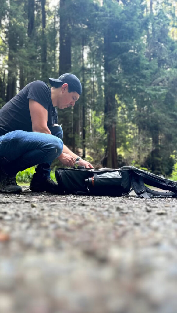 Photographer Dan Berger checking his camera bag during an engagement session amidst redwoods.