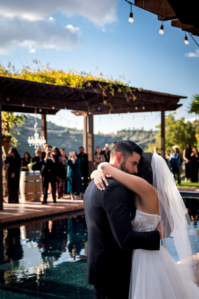 Bride and groom embrace during their first dance by the pool at Airola Road Vineyard in Murphys, CA, surrounded by twinkling lights and a beautiful outdoor setting.