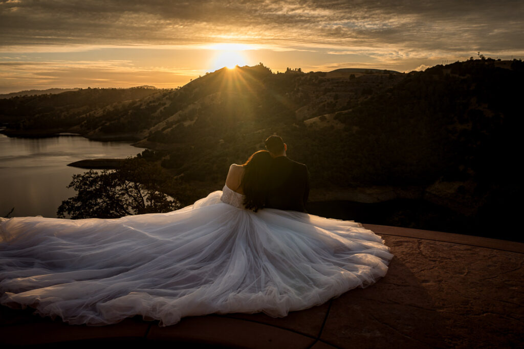 Bride and groom sit together during golden hour at Airola Road Vineyard, Murphys, CA, with the sun setting over the Sierra Foothills, creating a dreamy and romantic wedding portrait.