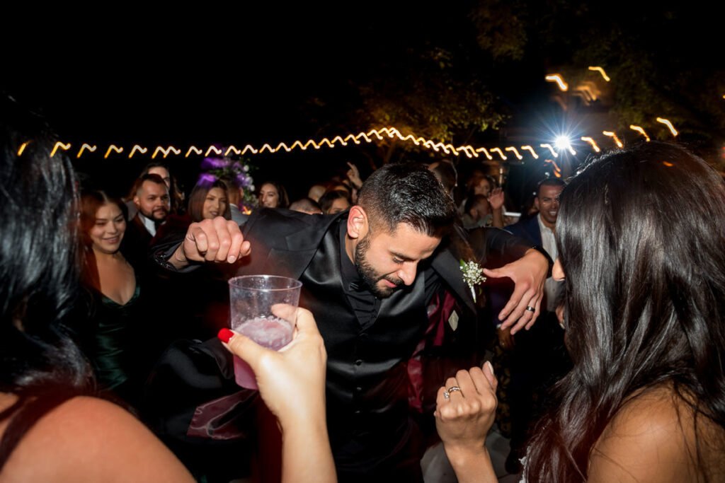 Groom dancing with guests at Airola Road Vineyard in Murphys, CA, during the wedding reception. Twinkling string lights and lively guests add to the high-energy celebration.